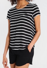 Top a maniche corte a righe bianche e nere con scollatura rotonda, vestibilità rilassata e tasca frontale. Abbinato a pantaloni corti neri.
