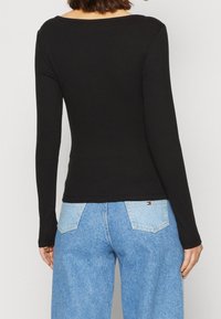 Schwarzes langärmliges Oberteil mit gerippter Textur und schulterfreiem Ausschnitt, kombiniert mit hellblauen weiten Jeans mit aufgesetzten Taschen.