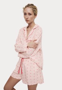 Rosa rutig pyjamasset i gingham med små röda hjärtan, med långärmad knäppning och shorts med elastiskt midjeband och dragsko.