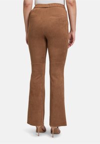 Brązowe spodnie z fauksu zamszowego w fasonie dzwonów, o gładkiej fakturze, z elastycznym pasem i dwiema tylnymi kieszeniami. Długość nogawki sięga powyżej kostek.