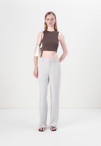 Brown cropped sleeveless top and light gray wide-leg trousers. The model holds a small white handbag. Sandals feature thin straps.
