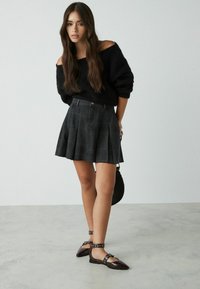 Sort fuzzy off-shoulder sweater, høj talje grå plaid plissee nederdel og sorte flade sko med spænder og metalliske detaljer.