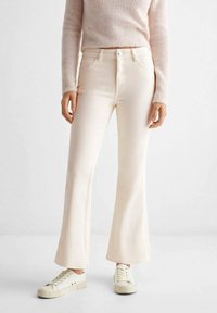 Jeans beige chiari a gamba larga con vita alta, tasche frontali e dettagli di cucitura sottili, abbinati a sneakers bianche.