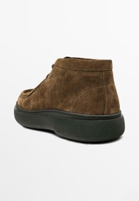 Bottines en suède marron avec un bout arrondi, dotées d'une semelle en caoutchouc noir rembourrée et de détails de coutures le long de l'empeigne.