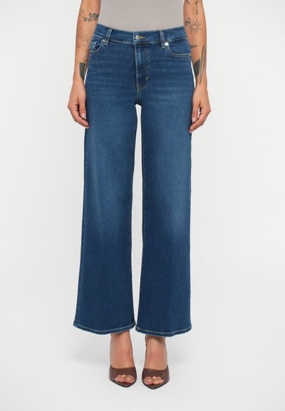 Jeans larges en denim bleu foncé, avec une taille haute, des poches traditionnelles et un léger délavage. L'ourlet a une finition à bords bruts.