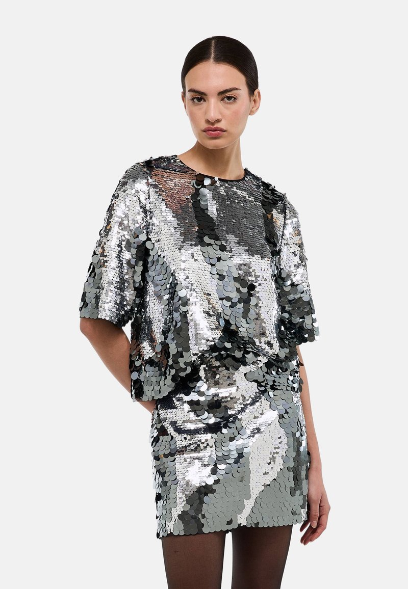 Haut à sequins argentés et noirs, coupe ample et manches courtes, assorti à une mini-jupe à sequins pour un effet brillant et réfléchi.