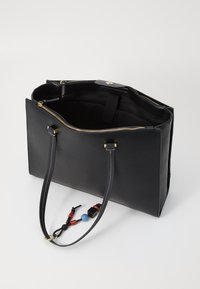 Sort læder tote taske med en struktureret form, gylden lynlås, dobbelte stropper og farverige dekorative charms hæftet til den ene håndtag.