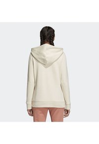 Krémová mikina s kapucí na šňůrku, žebrovanými manžetami a spodním lemem, volnějšího střihu, vyrobená z měkkého materiálu.