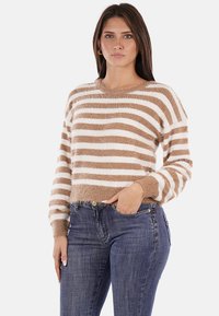 Maglione a righe marroni e bianche con una texture morbida, scollo tondo e polsini a coste, abbinato a jeans blu scuro.