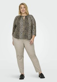 Bluse mit Leopardenmuster und Schlitzdetails, Dreiviertelärmel, kombiniert mit hellbeigen, taillierten Hosen und schwarzen Slippers.