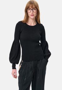 Czarny prążkowany sweter z bufkami, okrągłym dekoltem i dopasowanym tułowiem. Połączony z plisowanymi czarnymi spodniami, z subtelnym detalem w postaci logo.