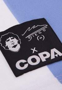 Copa-patch med hvid tekst på sort baggrund, der viser et grafisk billede af Diego Maradonas ansigt og signatur, sat mod blåt og hvidt stof.