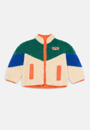 Casaco felpudo de fecho éclair com parte superior verde, corpo creme, remendos de mangas azuis, detalhe laranja e um patch de "disco" no peito, disposto plano sobre fundo branco.