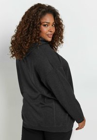 Sudadera gris oscuro de gran tamaño con cuello alto, hombros caídos y puños acanalados. Tela suave con un ajuste relajado.