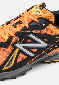 Svart och orange löparsko med meshuppvikning, gummisåle och grå detaljer. Har en framträdande "N" logotyp och kontrasterande snören.