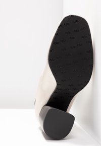 Béžová lodička na vysokém podpatku se hladkým svrškem, zaoblenou špičkou a černou texturovanou podrážkou se vzorem loga.