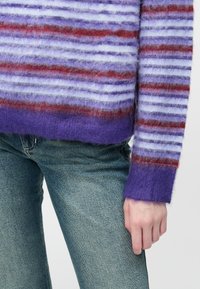 Jasnofioletowy sweter z dzianiny z czerwonymi i niebieskimi poziomymi paskami, o teksturowanym wykończeniu i ściągaczami, zestawiony z jasnobłękitnymi dżinsami.
