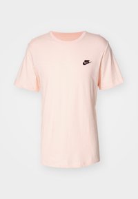 Jasnoróżowa bawełniana koszulka z krótkim rękawem, okrągłym dekoltem i małym czarnym haftowanym logo Nike po lewej stronie klatki piersiowej.