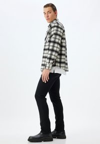Camisa de cuadros en blanco y negro, de tela ligera, combinada con jeans ajustados negros y botas negras hasta el tobillo. Textura suave, estilo casual.