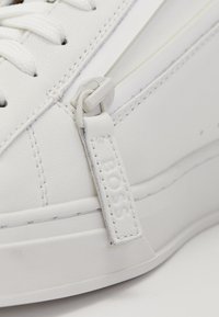 Λευκά παπούτσια με σμαλτμένη δερματίνη, με στρογγυλή μύτη, επίπεδους κορδόνια και ετικέτα λογότυπου. Υφή σόλας και διακριτές ραφές.