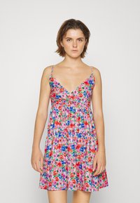 Vestido floral com decote em V, alças finas e design de camadas com babados. Apresenta flores vibrantes em vermelho, azul e rosa sobre um fundo claro.