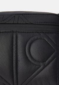 Zwart gevoerd stof met geometrische patronen, met afgeronde vormen en subtiele stitching details, creëert een getextureerd visueel effect.