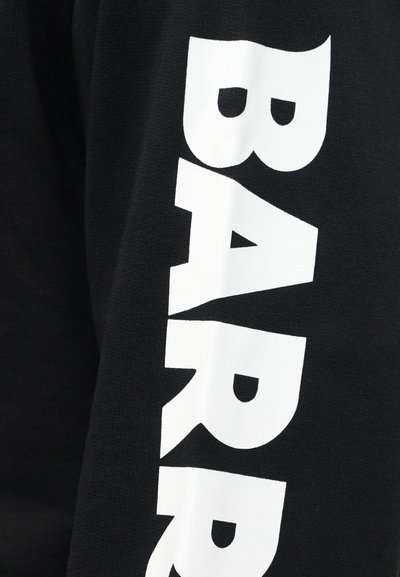 Svart stoff med stor, vertikal, fet hvit tekst som lyder "BARR" på ermeområdet av et plagg.