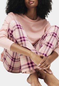 Hellrosa Langarmshirt kombiniert mit rosa-lila karierten Schlafanzughosen, die einen weichen Baumwollstoff und eine lockere Passform aufweisen.