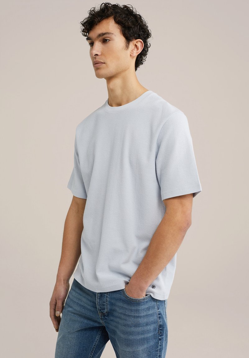 Ljusblå kortärmad t-shirt i en strukturerad tygkvalitet med rundad halsringning, kombinerad med blå jeans och en diskret logodetalj längst ner.