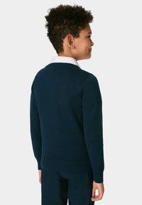 Pull en maille bleu marine avec un ourlet et des poignets côtelés. Il présente un col rond et une texture lisse, porté par-dessus une chemise blanche à col.