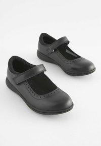 Zapatos Mary Jane de cuero negro con punta redondeada, detalles perforados y correa ajustable. Suela plana para mayor comodidad.