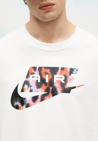 Tuva skatījums uz personu, kas valkā baltu kreklu ar krāsainu, rakstainu Nike Air logo uz krūtīm.