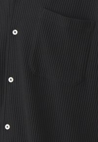 Mustamärkidega särk ribakonstruktsiooniga, millel on üks rinnaTasku ja valged nööbid, rõhutades vabamat disaini.