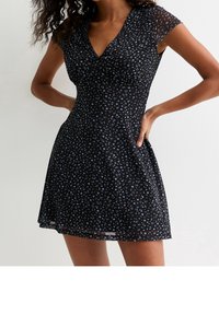 Černé květinové šaty s krátkými průsvitnými rukávy, výstřihem do V a přiléhavým živůtkem. Obsahují malé modré květy rozptýlené po celém povrchu.