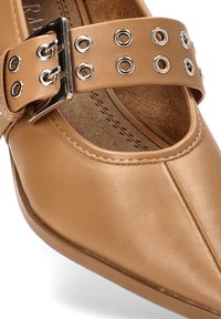Zapato de cuero marrón con punta afilada, presenta una correa ancha con recortes circulares y una hebilla plateada como acento.
