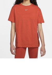 Person som bär en rostfärgad T-shirt med kort ärm från Nike och matchande leggings, båda med små vita Nike swoosh-logotyper.