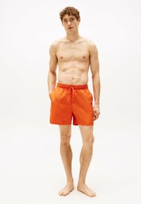 Costumi da bagno arancioni realizzati in materiale leggero, dotati di vita elasticizzata e lacci. Sono visibili due tasche laterali.