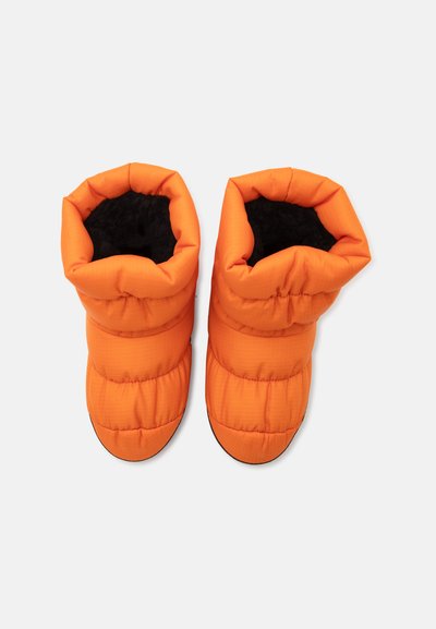 Paire de chaussons d'intérieur orange matelassés avec une doublure intérieure douce noire, vue de dessus sur un fond clair uni.