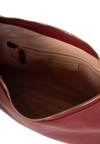 El interior de la bolsa de cuero rojo presenta un forro suave, un cierre dorado y un bolsillo interior con una etiqueta de cuero que dice "Coccinelle, Cuero Italiano Auténtico."