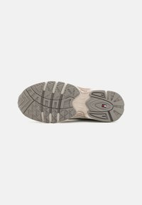 Podeszwa sneakersów w beżowo-szarym kolorze, z gumowym wzorem, teksturowana w różne wzory i rowki dla lepszej przyczepności, z małym detalem logo.