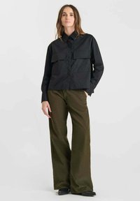 Black button-up shirt with two chest pockets, paired with olive wide-leg pants. Shirt has a smooth texture; pants feature a corduroy finish.