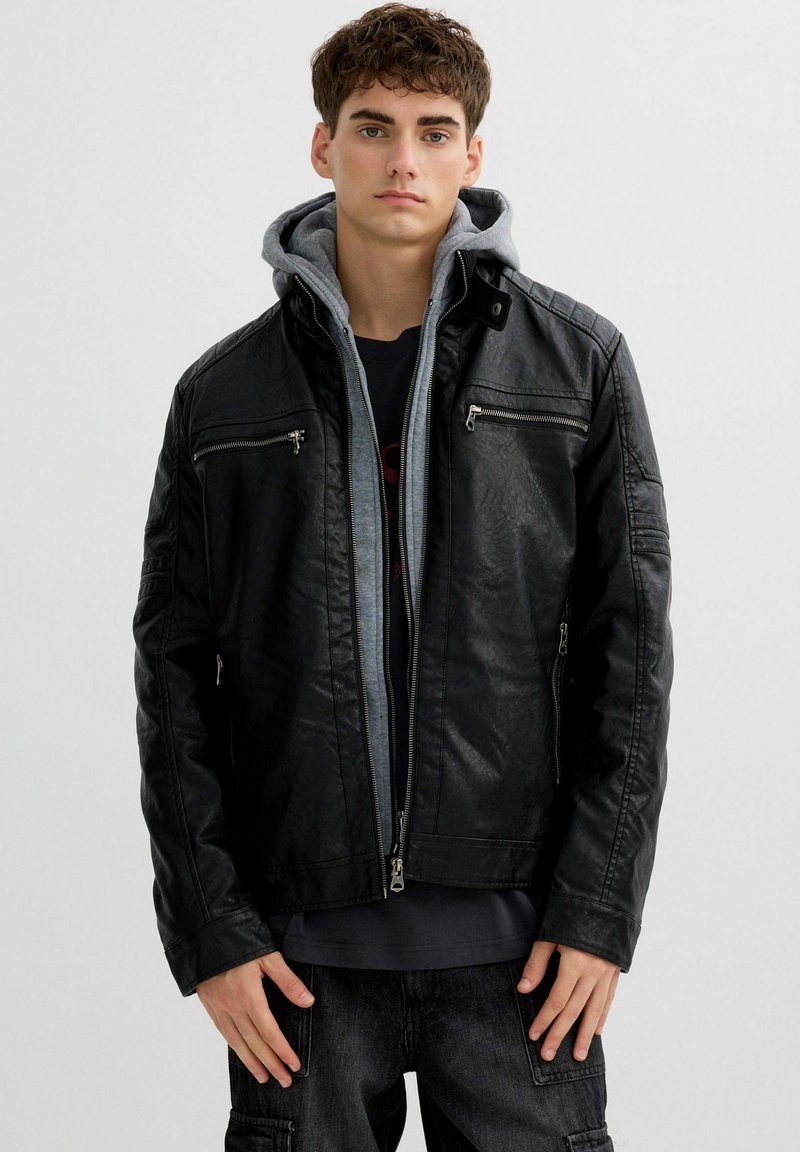 Chaqueta de piel negra con bolsillos con cremallera, sudadera gris debajo y una textura suave. La chaqueta cuenta con un cuello alto y un diseño ajustado.
