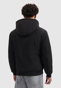 Zwarte gevoerde jas met een capuchon, voorzien van een gladde textuur, ribbelmanschetten en -zoom, en minimale stikdetails op de achterkant.