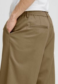 Khaki broek met een elastische tailleband, zijzakken en twee achterzakken met paspel. De stof heeft een gladde, gestructureerde afwerking.