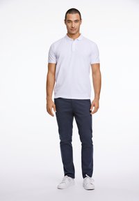 Polo bianco, maniche corte, colletto con bottoni. Pantaloni scuri blu navy, taglio slim. Sneakers bianche, texture liscia. Design semplice e pulito.