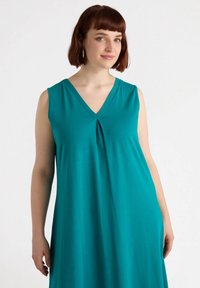 Turkosärmlös klänning med V-ringning och plisserad frontdetalj, gjord av ett slätt tyg, som faller mjukt till midkalvlängd.