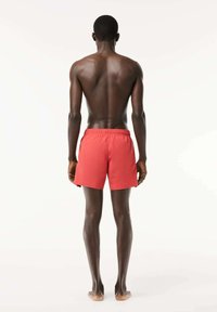 Costume da bagno rosso con vita elastica, caratterizzato da una texture liscia e una lunghezza fino alla metà della coscia, mostrato da dietro.