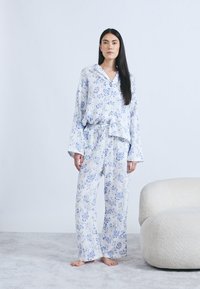 Ensemble pyjama léger à fleurs en blanc et bleu, avec manches larges, coupe ample et taille à cordon pour le pantalon. Texture douce.