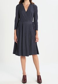 Navy wrap-mekko, jossa on valkoisia pilkkuja, V-pääkallo, pitkät hihat ja laskostettu hame. Yhdistetty marooninvärisiin nilkkasaappaisiin. Suuni kankaan tekstuuri.