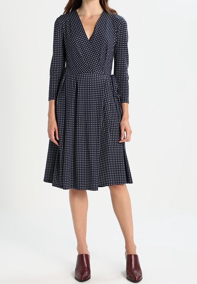 Navy wrap-mekko, jossa on valkoisia pilkkuja, V-pääkallo, pitkät hihat ja laskostettu hame. Yhdistetty marooninvärisiin nilkkasaappaisiin. Suuni kankaan tekstuuri.